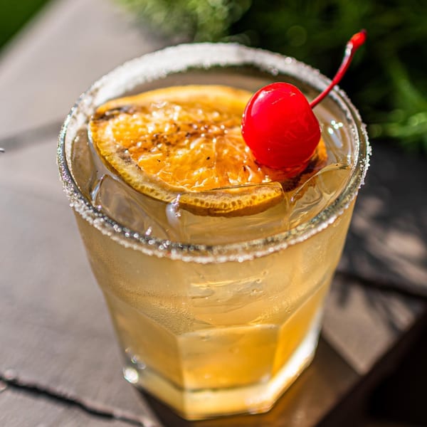 ZOCALO's margarita with a salted rim, garnished with a charred orange slice and a red cherry.