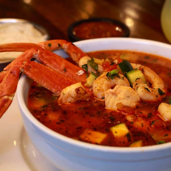 ZOCALO's vibrant seafood soup with crab legs, shrimp, and vegetables in a white bowl.