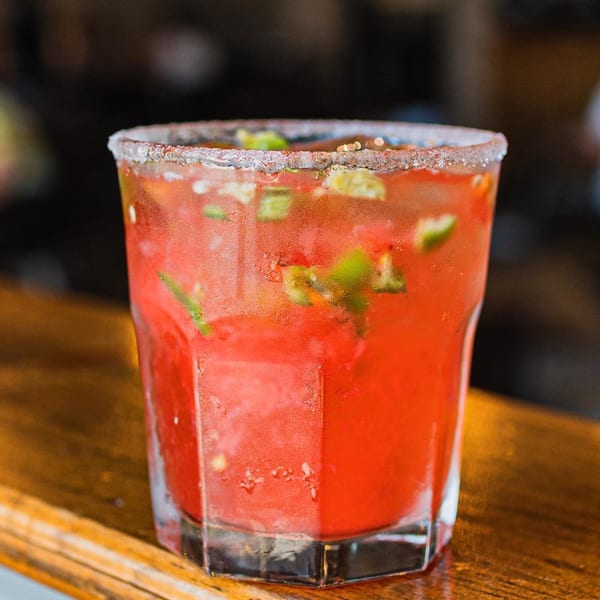A vibrant red ZOCALO Mexican cocktail with jalapeño, ice, and a salted rim on a wooden bar.