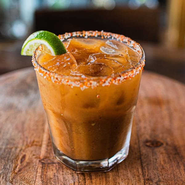 ZOCALO's michelada cocktail with a chili-salt rim and lime wedge on a wooden table.