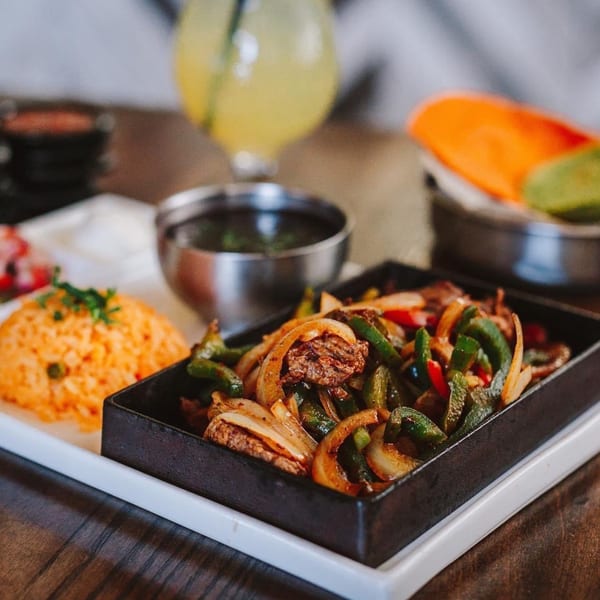 ZOCALO's sizzling fajitas with steak, peppers, and onions, served with rice and black beans.