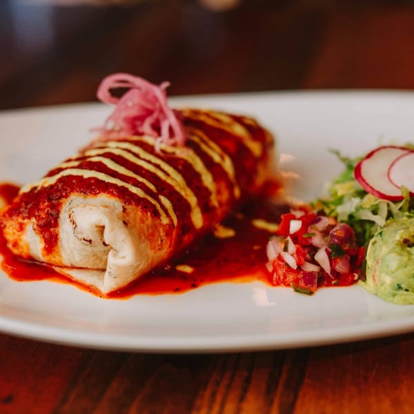 A ZOCALO Mexican burrito covered in red and yellow sauce, with guacamole and pico de gallo.