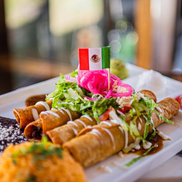 ZOCALO's taquitos with lettuce, pickled onions, crema, and a small Mexican flag.