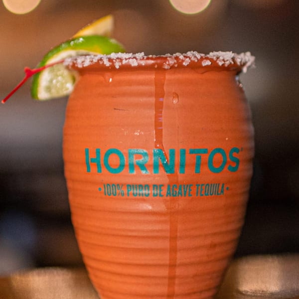 A Hornitos tequila drink in a terracotta mug, garnished with lime and a cherry, rimmed with salt.
